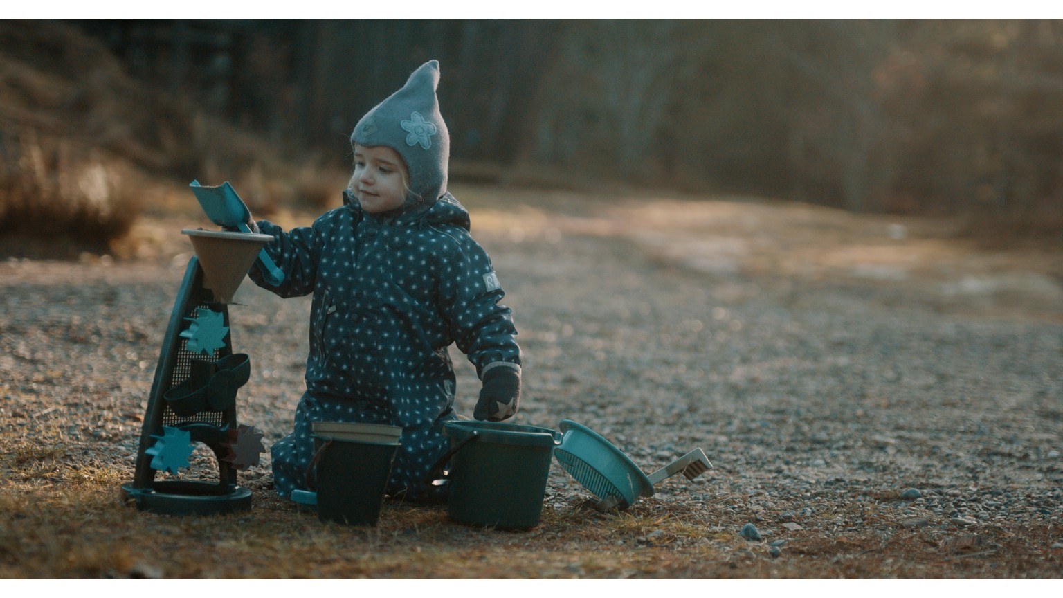 Barn i vinterdress leger med blå vandmølle på sandet jord i skumringen